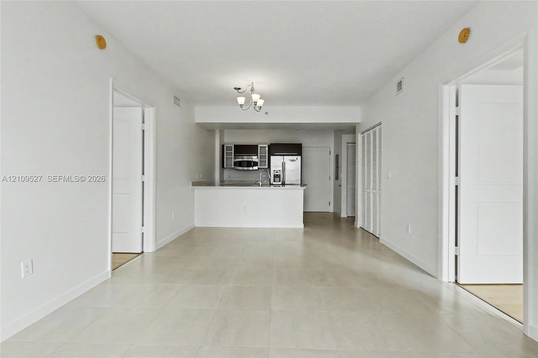Open-concept floor plan featuring large-format ceramic tile flooring, a kitchen peninsula, ceiling-mounted multi-light fixture, and bi-fold closet doors