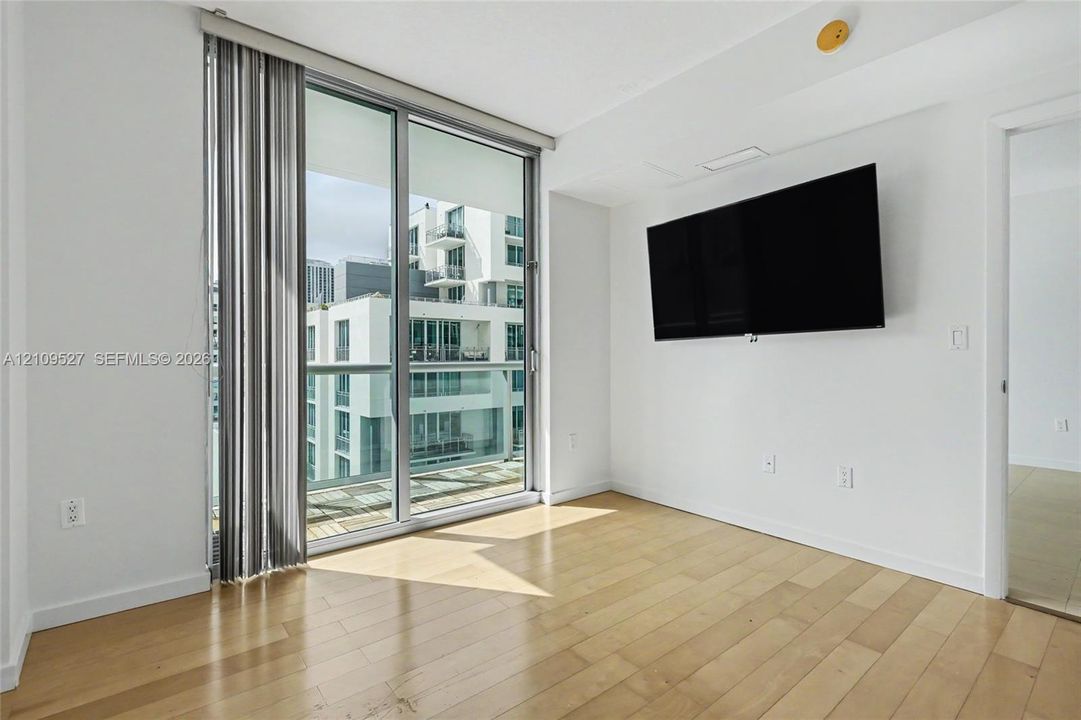 Floor-to-ceiling glass sliding doors opening to an exterior balcony, light-toned wood-finish flooring, and white walls