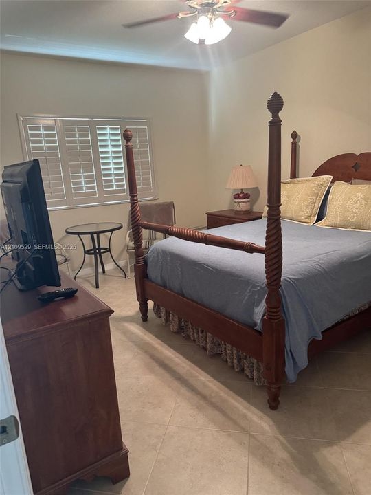 Interior room featuring neutral wall paint, large-format tile flooring, white plantation shutters, and a ceiling-mounted light fixture with a fan