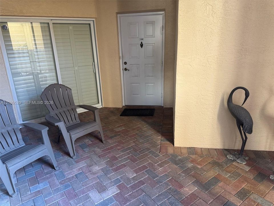 Covered patio featuring multi-toned herringbone brick pavers, recessed entry door with multi-panel detailing, and integrated sliding glass door