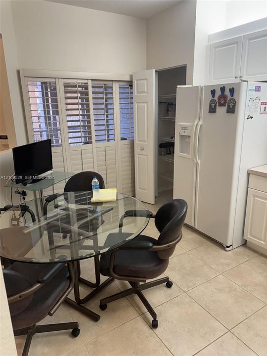 Kitchen featuring white shaker-style cabinetry, a built-in pantry with wire shelving, ceramic tile flooring, and louvered window shutters