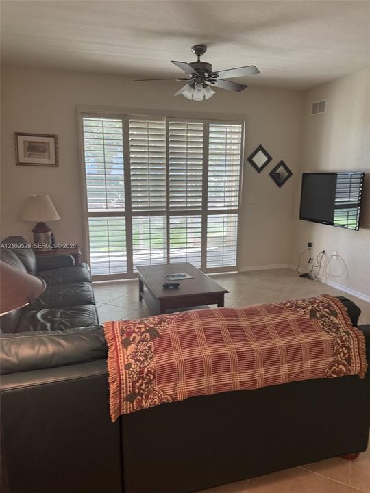 Large sliding glass doors featuring white plantation shutters, tile flooring, and a ceiling fan with integrated lighting