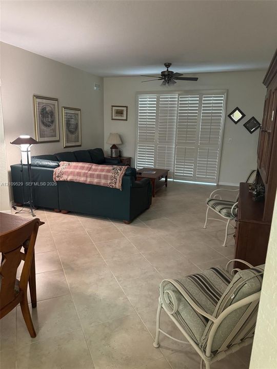 Large-format tile flooring, ceiling fan with light fixture, and floor-to-ceiling plantation shutters