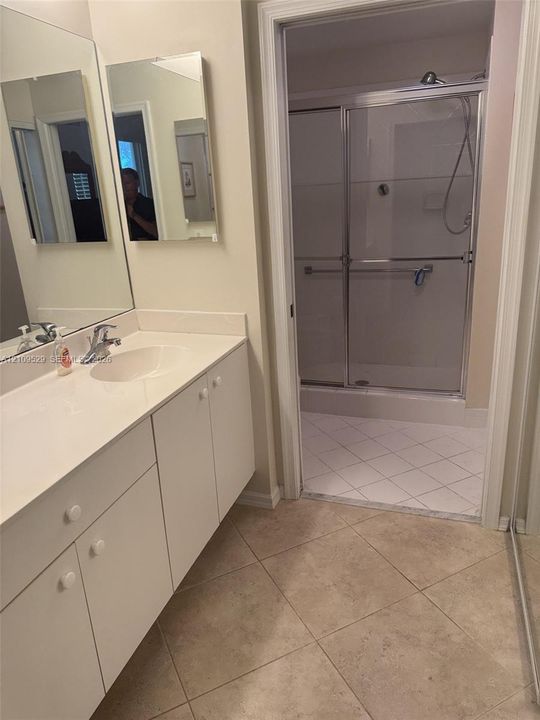 Bathroom featuring a long vanity with white cabinetry, a large wall-mounted mirror, and a walk-in shower with a sliding glass door and tile flooring