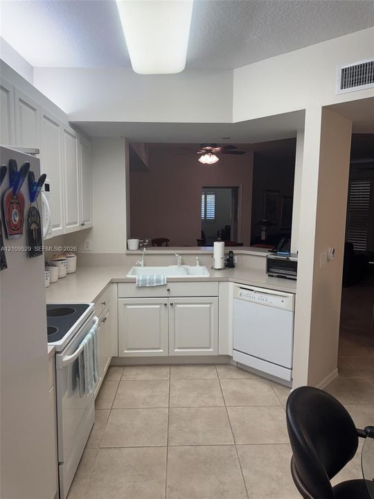 Kitchen featuring white cabinetry, solid surface countertops, an integrated double-basin sink, built-in dishwasher, and ceramic tile flooring