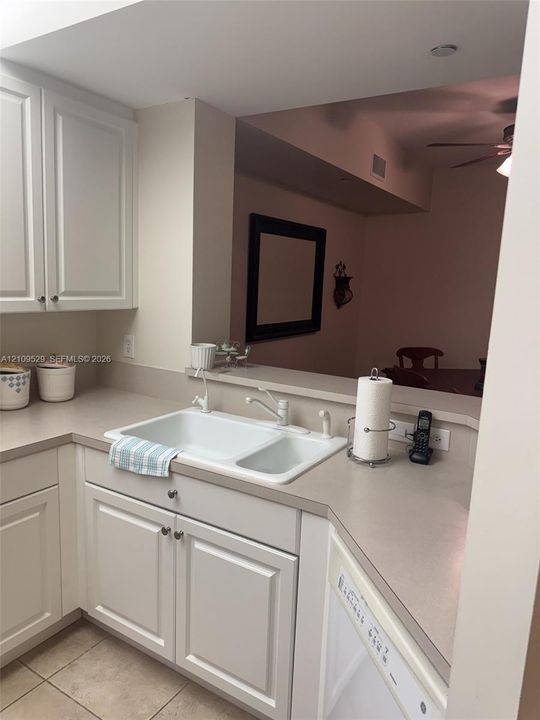 Kitchen featuring white shaker-style cabinetry, solid-surface countertops, a double-basin undermount sink, and tile flooring
