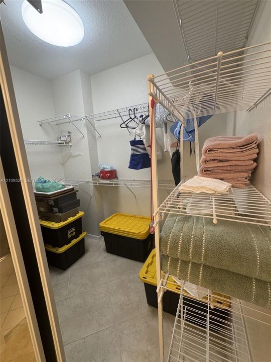 Walk-in storage space featuring ceramic tile flooring, ceiling-mounted lighting, and tiered white wire shelving