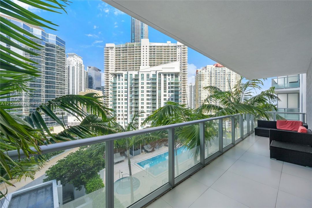 Covered balcony with large-format tile flooring and a glass-paneled railing overlooking an outdoor pool and spa area