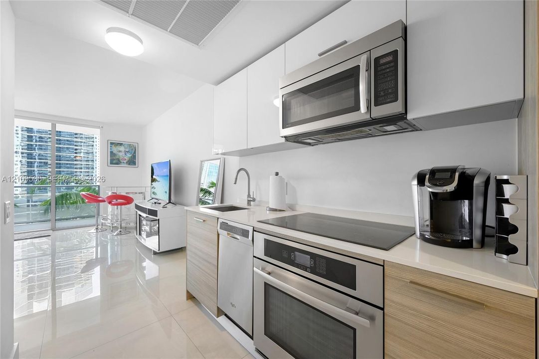 Kitchen featuring white gloss upper cabinetry, wood-finish lower cabinetry, solid surface countertops, stainless steel appliances, and integrated cooktop