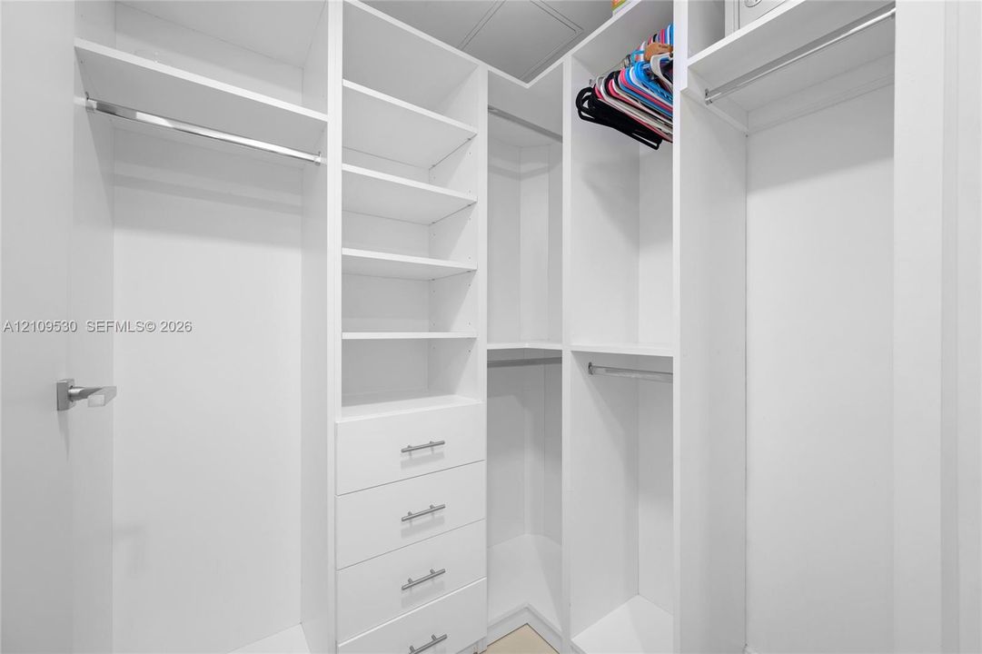 Custom walk-in closet featuring white built-in shelving, four integrated storage drawers with brushed metal pulls, and multiple tiered hanging rods