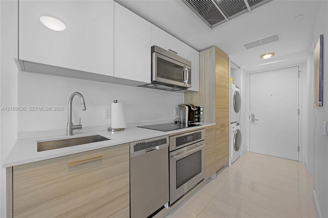 Kitchen featuring two-tone cabinetry with wood-finish lower cabinets and white upper cabinets, white solid surface countertops, stainless steel appliances, and tile flooring