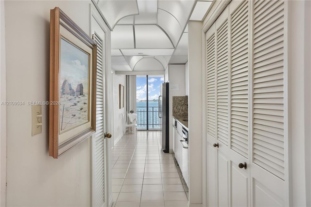 Hallway featuring white tile flooring, louvered closet doors, and a vaulted ceiling, leading to a balcony with water scenery