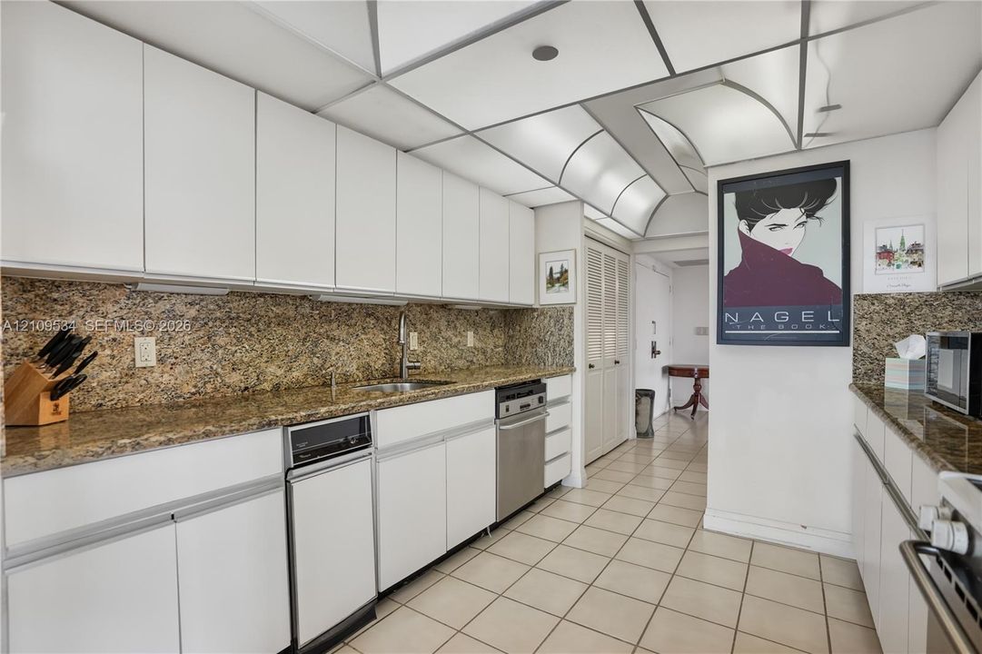 Kitchen featuring white flat-panel cabinetry, stone countertops, tiled flooring, integrated lighting, and stainless steel appliances