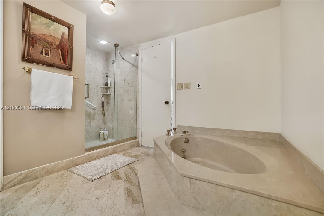 Jetted soaking tub with a stone-surround deck, walk-in shower enclosed by a frameless glass door, and stone tile flooring