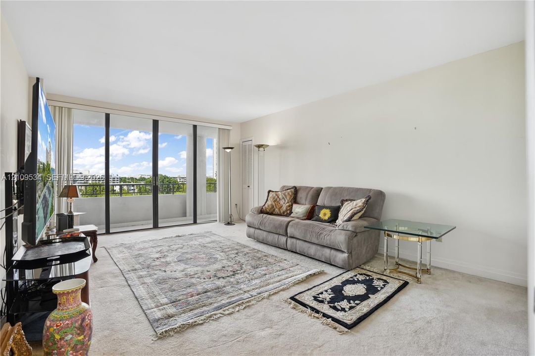 Living area featuring neutral carpeting, expansive floor-to-ceiling glass sliding doors, and a private balcony