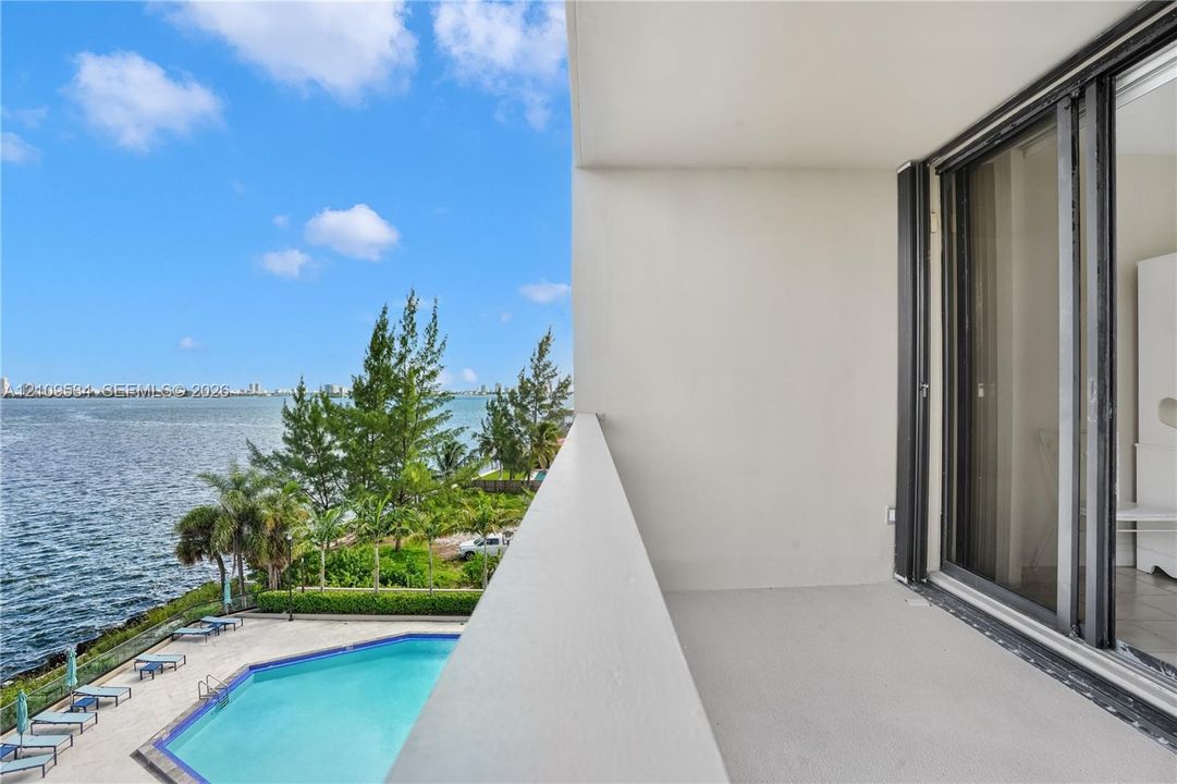 Covered balcony featuring sliding glass doors, solid wall railings, and exterior flooring, with a clear expanse of water and a swimming pool below