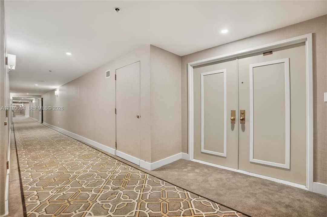 Hallway featuring recessed ceiling lighting, textured wall coverings, double doors with metallic hardware, and patterned carpeting