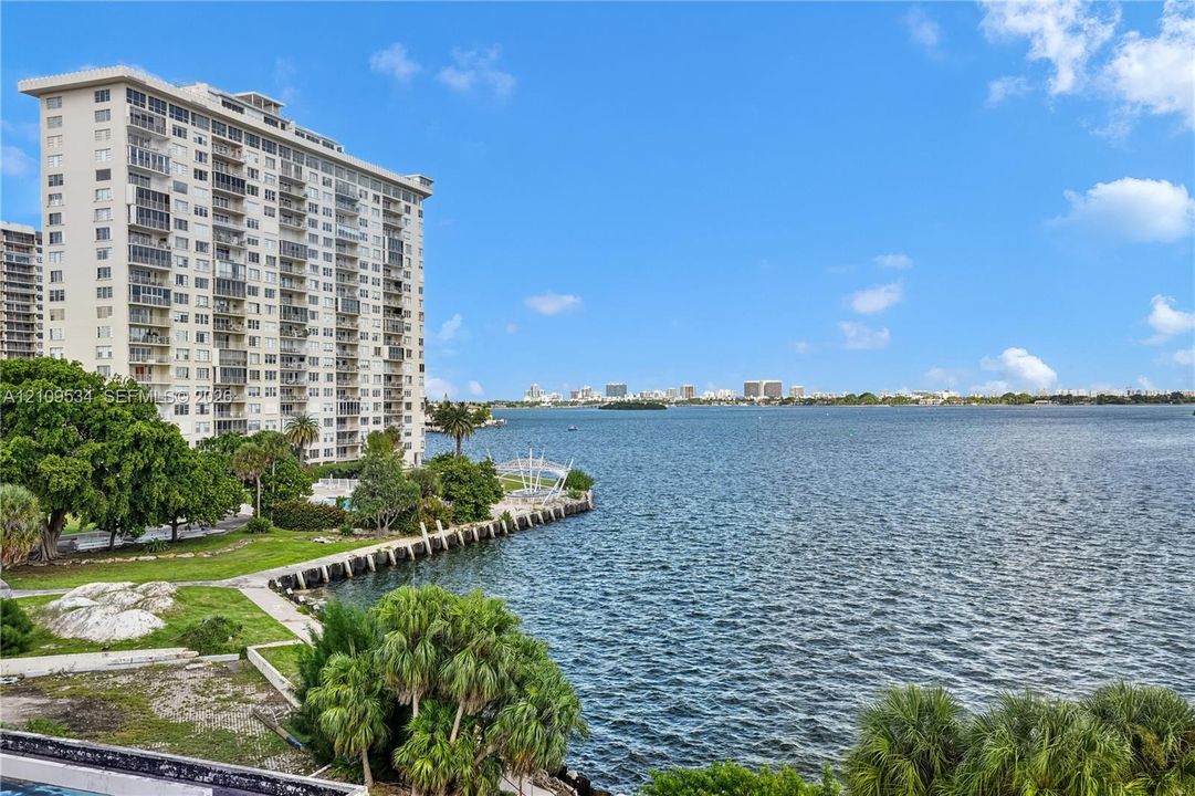 High-rise residential exterior with water frontage, concrete bulkhead, mature landscaping, and palm trees