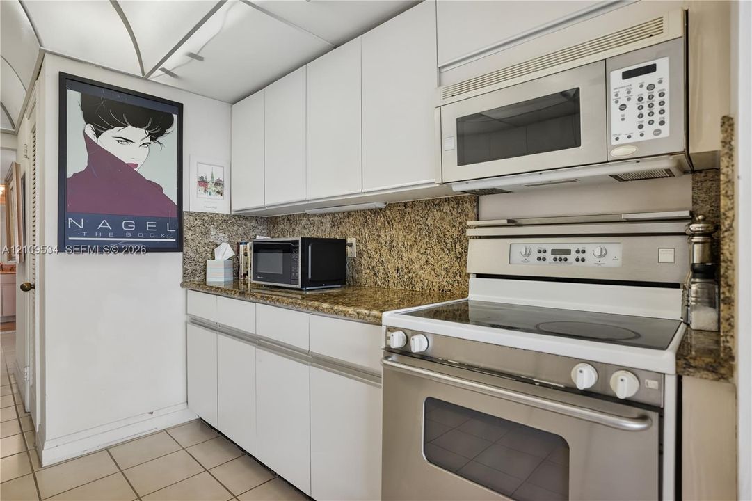 Kitchen featuring flat-panel white cabinetry, stone countertops, tiled flooring, and stainless steel appliances including an over-the-range microwave and electric range