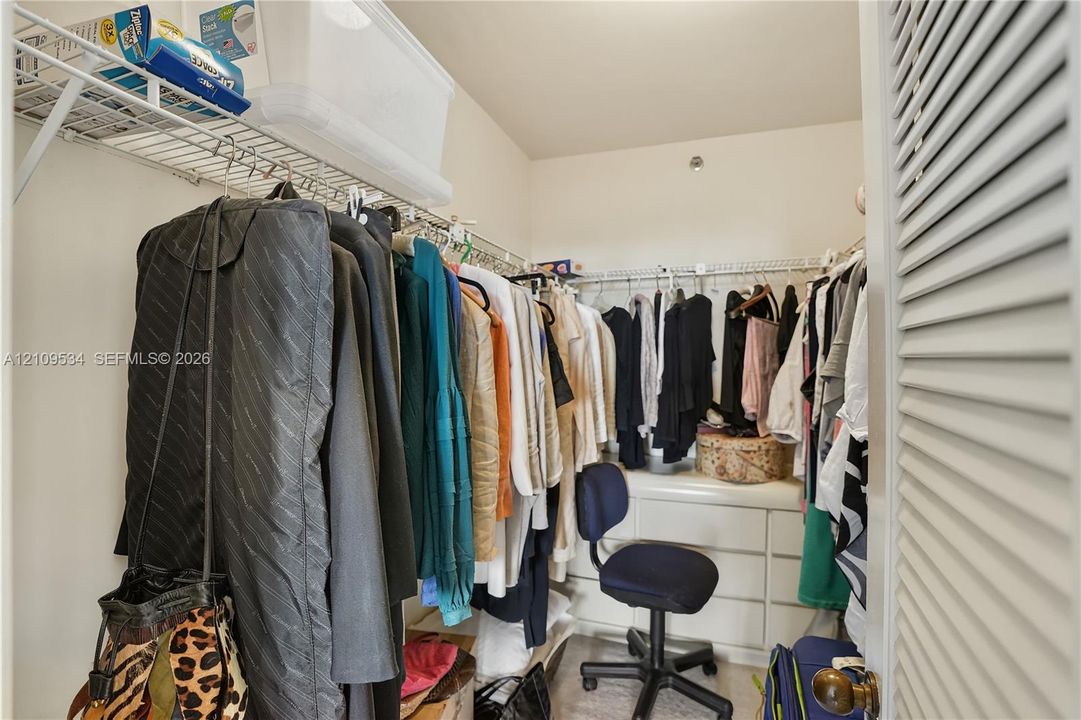 Walk-in closet featuring built-in white cabinetry, tiered metal shelving, and louvered door entry