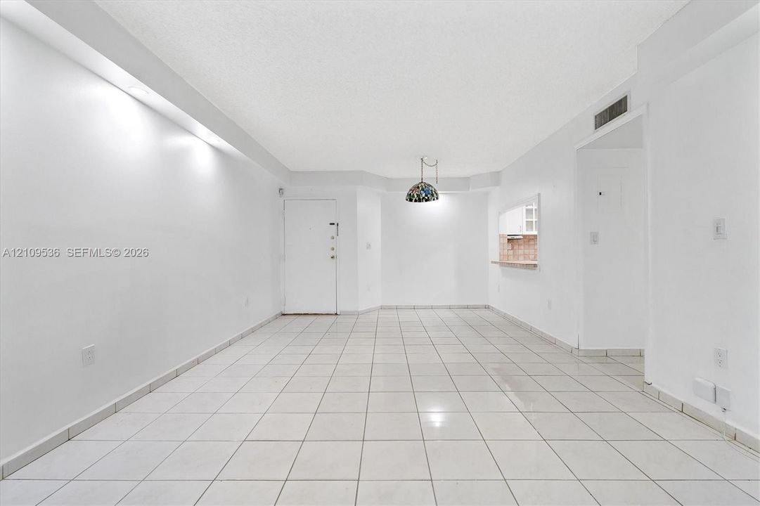 Interior space featuring neutral tile flooring, recessed ceiling lighting, a decorative hanging pendant fixture, and a pass-through window with an integrated counter
