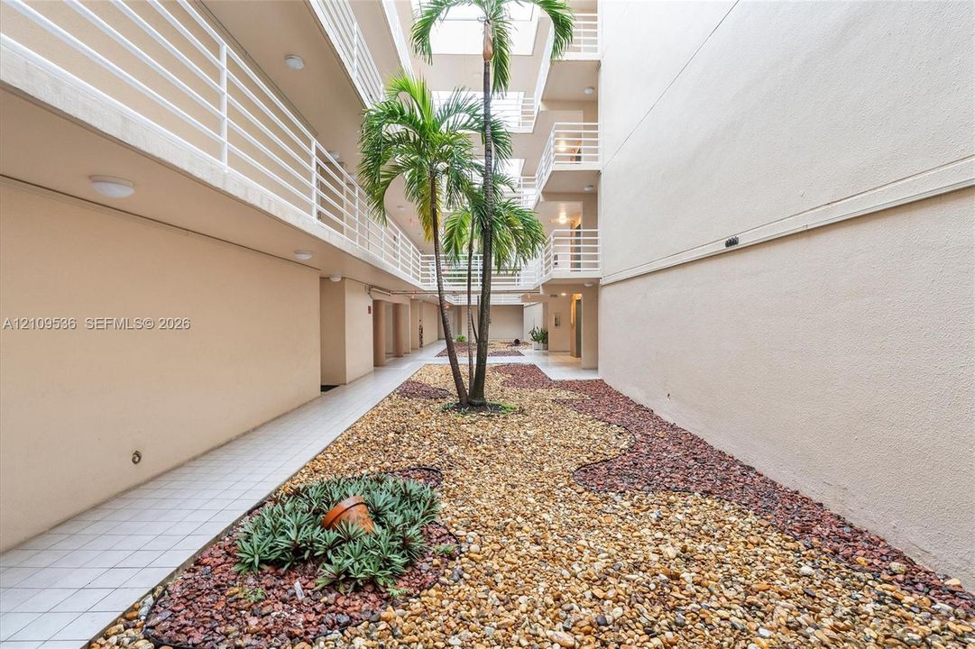 Open-air central courtyard featuring multi-story balustrades, rock landscaping, mature palms, and tiled walkways