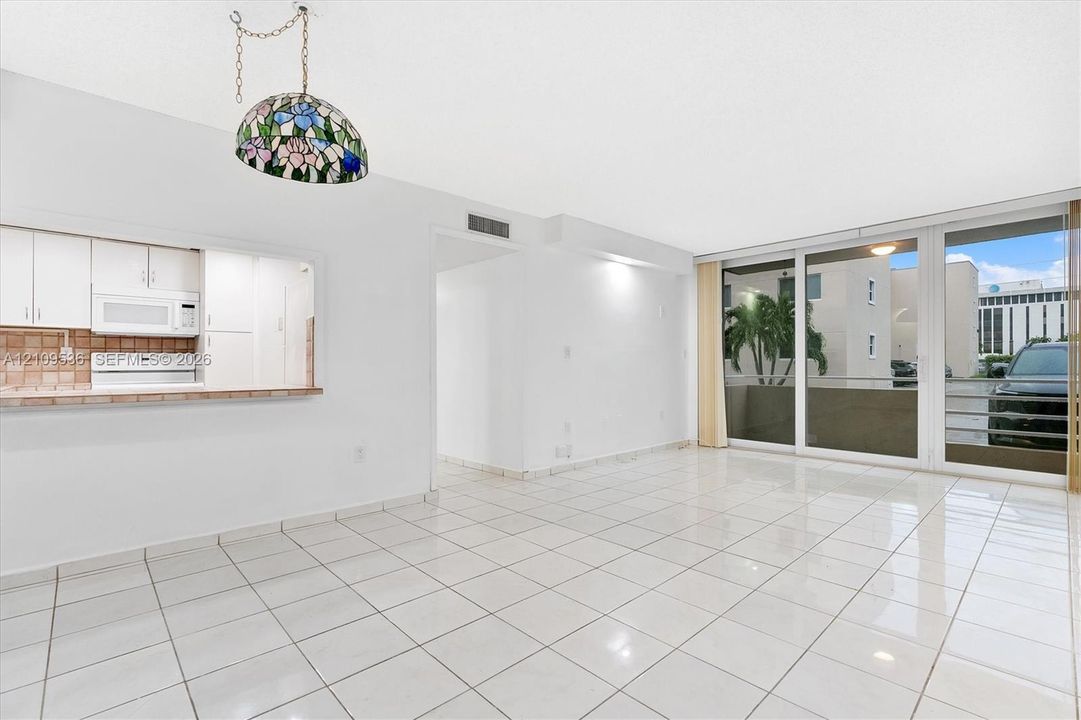 Open living area featuring white tile flooring, large glass sliding doors, built-in kitchen cabinetry with a serving pass-through, and a decorative stained-glass pendant light fixture