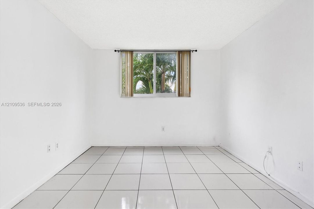 Room featuring large-format white tile flooring, neutral wall finishes, and a window with exterior foliage