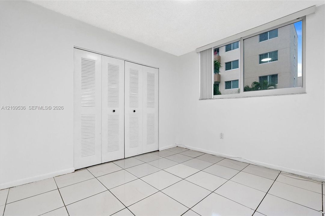 Neutral-toned room featuring large-format tile flooring, dual louvered-panel closets, and a sliding glass window