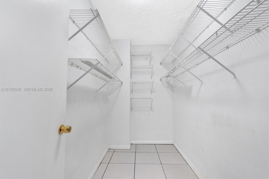 Walk-in storage space featuring ceramic tile flooring, tiered white wire shelving, and a brass-tone door handle