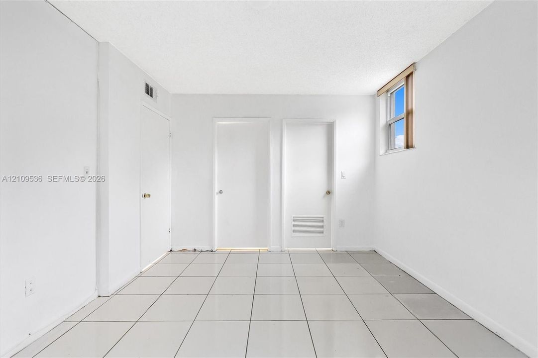 Interior space featuring neutral tile flooring, two solid-core interior doors, one closet with a white panel door, and an upper-wall window