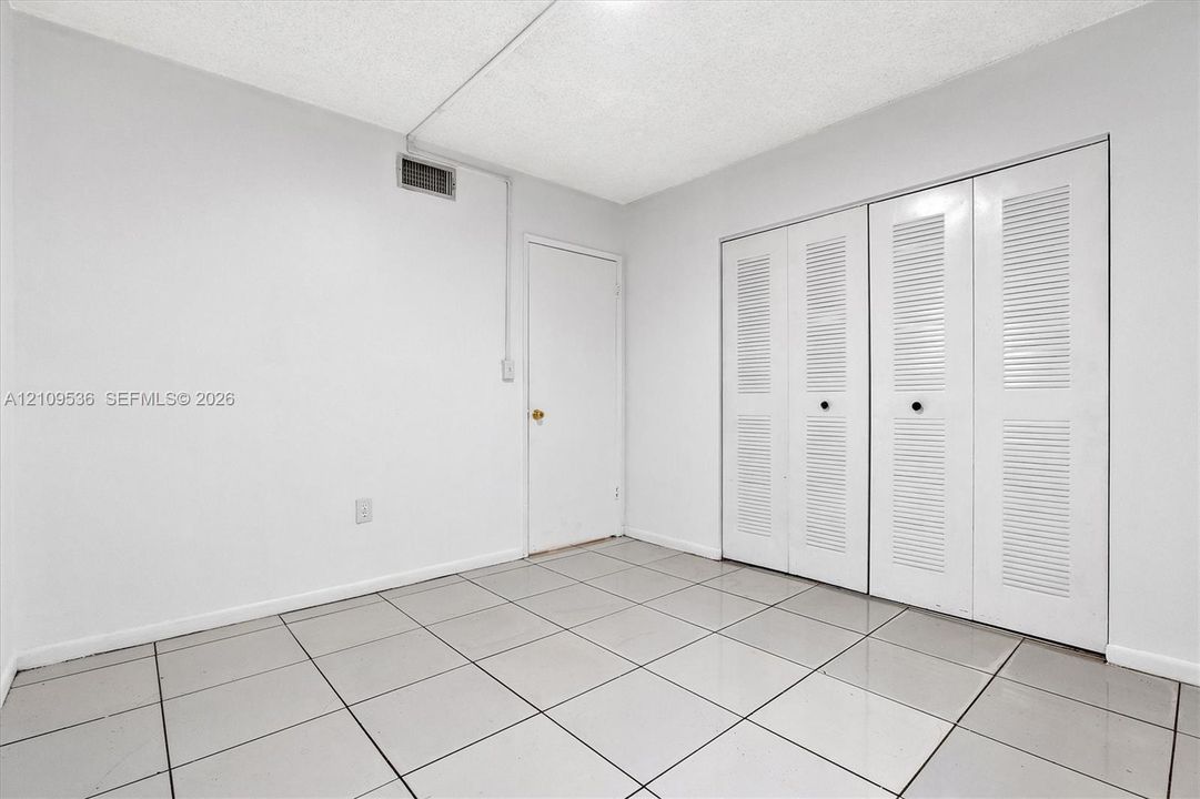 Neutral-toned tiled flooring, white interior walls, and dual white louvered-door closets