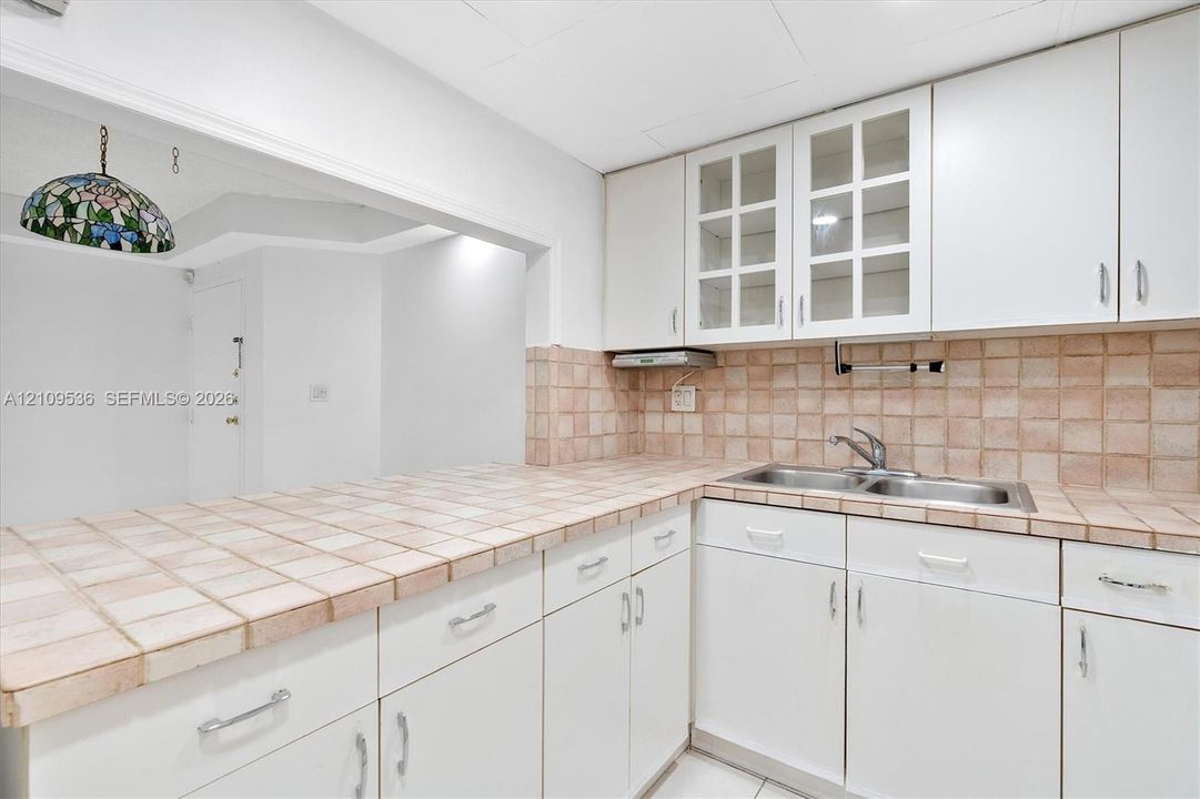 Kitchen featuring white cabinetry, glass-front upper cabinet doors, tiled countertops, a tiled backsplash, and a double-basin stainless steel sink
