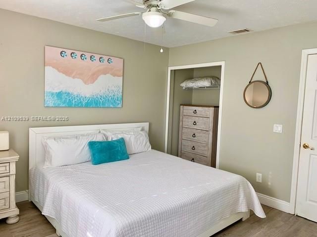 Ceiling fan with integrated lighting, wood-finish flooring, and a built-in closet with shelving