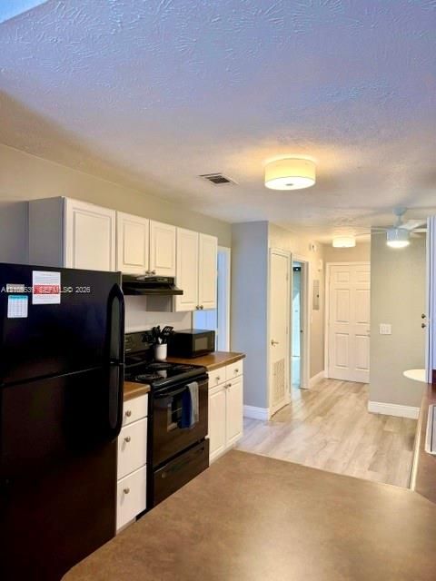 Kitchen featuring white cabinetry, black appliances, brown countertops, and wood-finish flooring