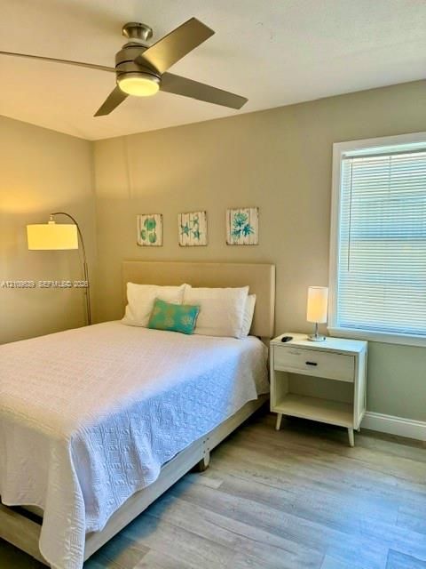Wood-finish flooring, ceiling fan with integrated lighting, window with blinds, and painted walls