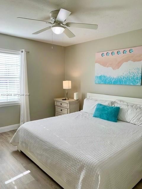 Wood-finish flooring throughout, ceiling fan with integrated lighting, window with blinds, and painted walls