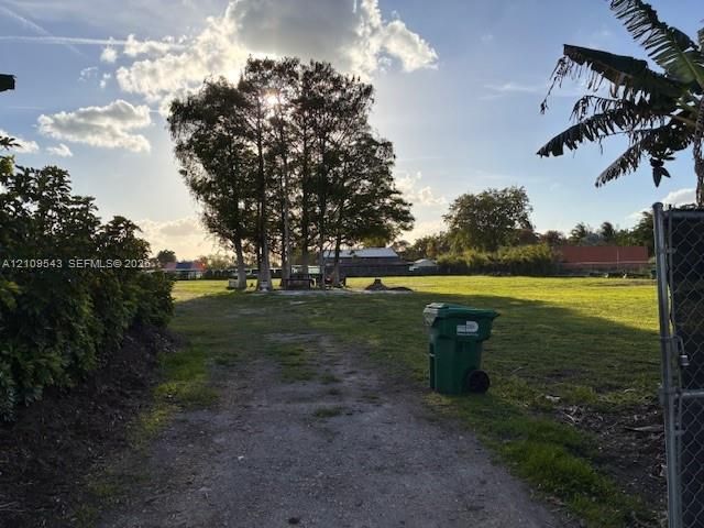 Expansive open lot featuring mature trees, a gravel access path, and established perimeter hedging