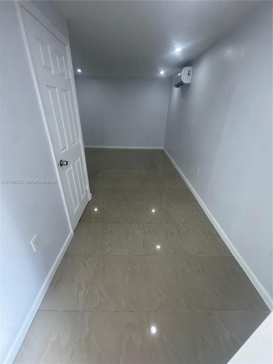 Interior space featuring neutral-tone ceramic tile flooring, recessed ceiling lighting, a wall-mounted ductless air conditioning unit, and a six-panel door