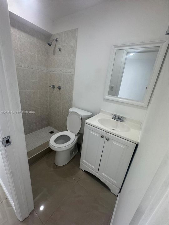 Bathroom featuring a white vanity cabinet with a integrated sink, framed wall mirror, walk-in shower with tiled surround, and large-format neutral flooring