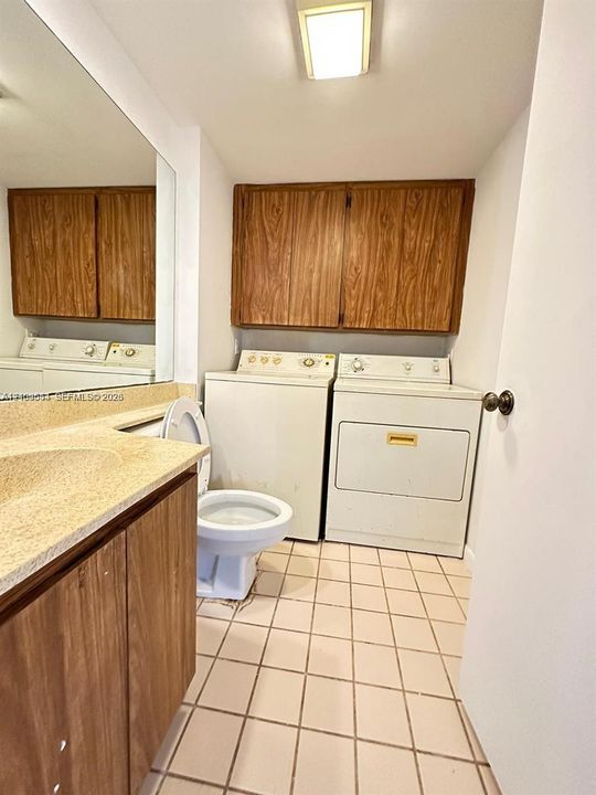 Utility space featuring ceramic tile flooring, built-in wood-finish cabinetry, a full-width vanity mirror, a countertop-integrated sink, and laundry hookups