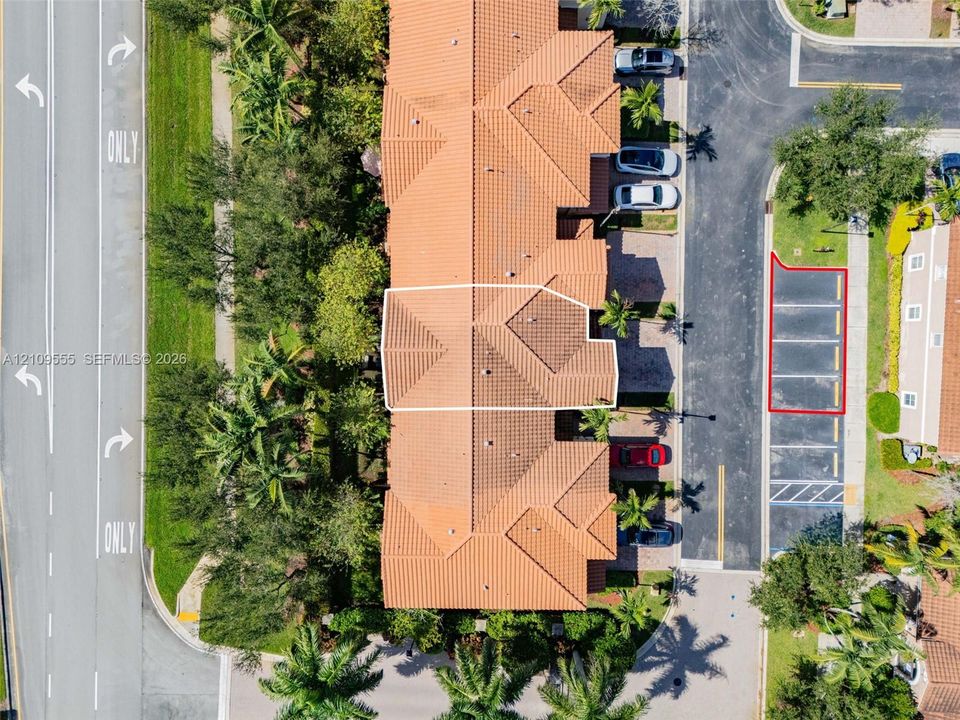 Aerial perspective of a multi-unit property featuring a clay tile roof, designated parking space, and mature landscaping