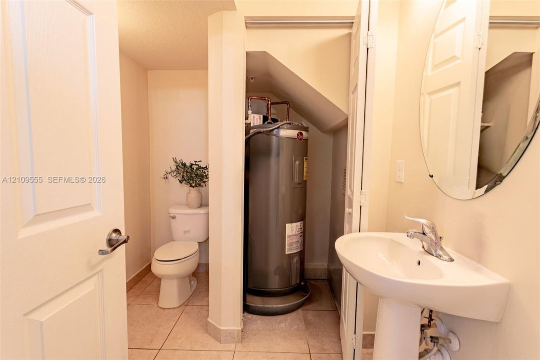Powder room featuring a pedestal sink with a chrome faucet, a rounded wall-mounted mirror, ceramic tile flooring, and an enclosed water heater