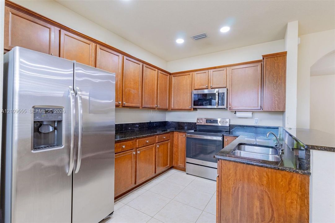 Kitchen featuring wood cabinetry, stone countertops, stainless steel side-by-side refrigerator, stainless steel electric range, and integrated microwave