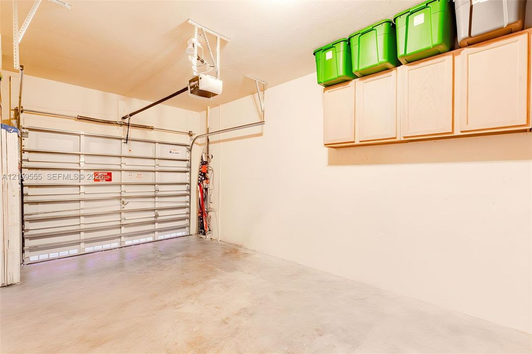 Garage interior featuring a sectional roll-up door, automated door opener, and wall-mounted light-finish storage cabinetry