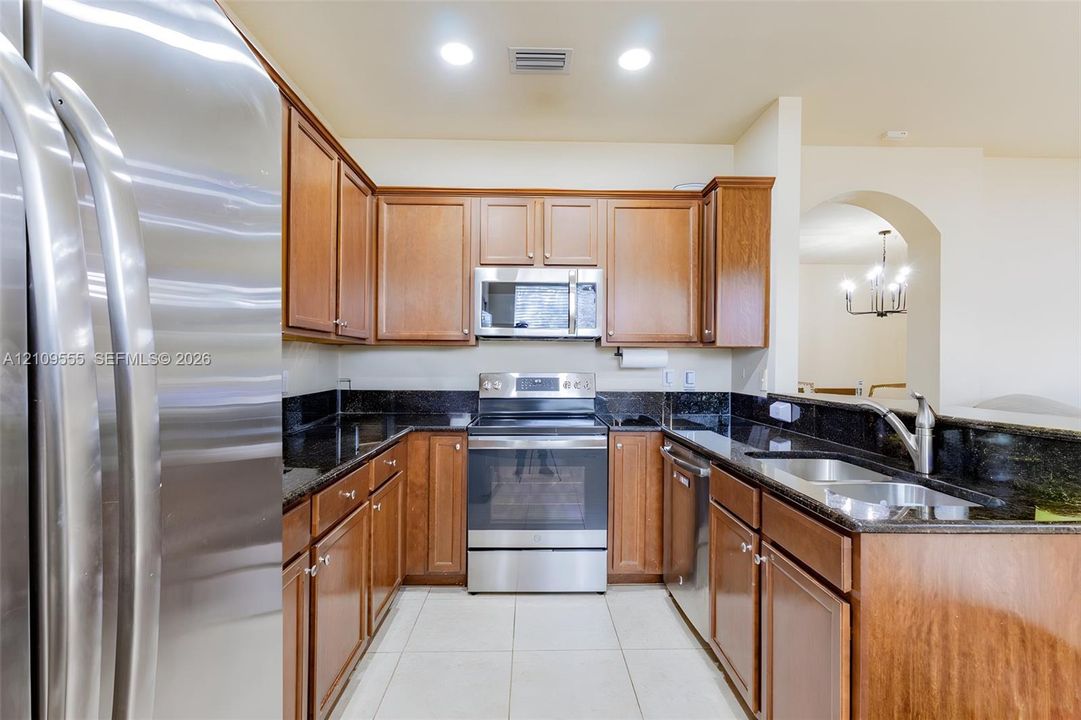 Kitchen featuring wood cabinetry, stone countertops, stainless steel appliances, a double-basin sink, and tile flooring