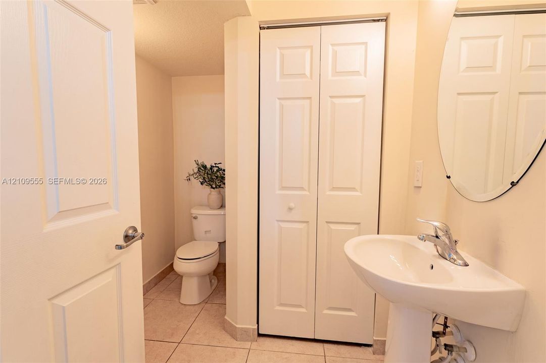 Pedestal sink with polished chrome faucet, oval wall-mounted mirror, white paneled bifold closet door, and tile flooring