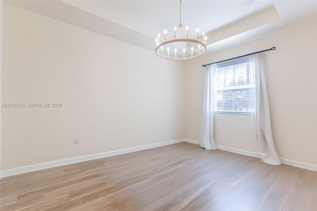 Tray ceiling featuring a large circular tiered chandelier, wood-finish flooring, and a window with a curtain rod