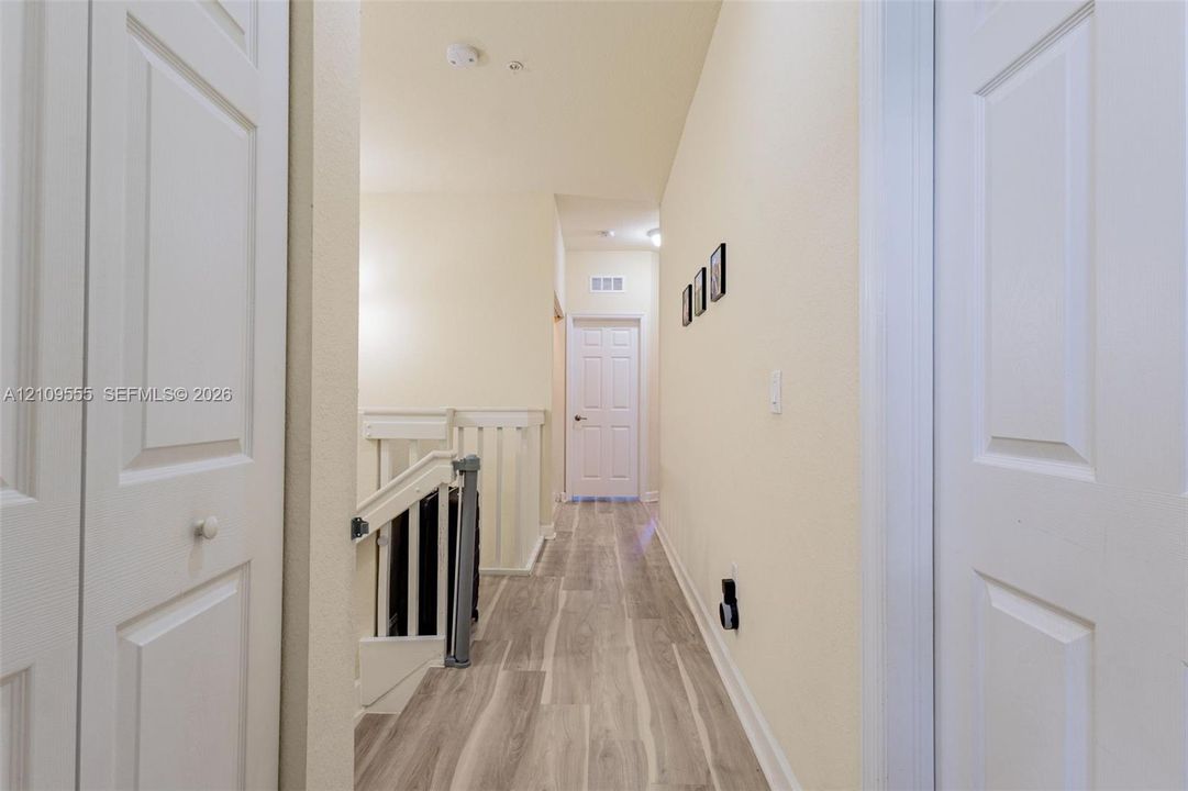 Hallway featuring wood-finish flooring, two sets of paneled closet doors, and a staircase with white painted balusters and railings