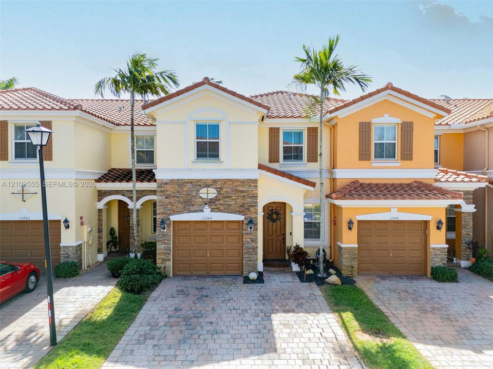 Stucco exterior with stone veneer accents, multi-tone tile roof, paver driveways, and individual attached garages